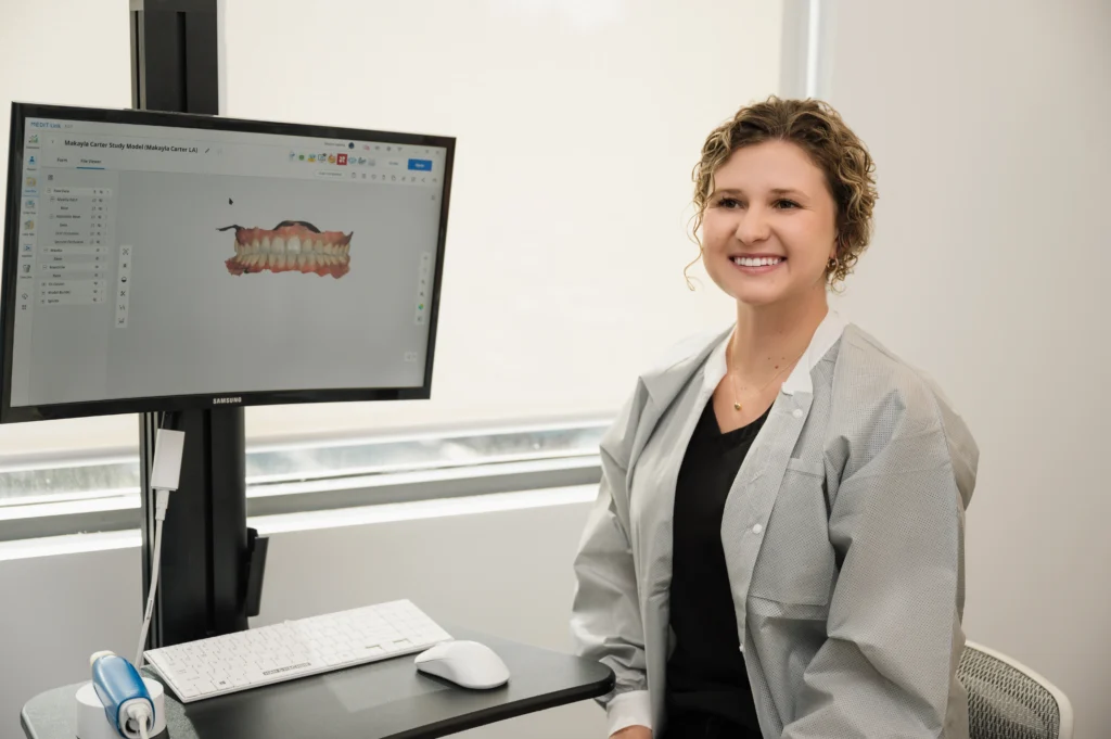 MaKayla sitting next to a display showing a 3D model of teeth smiling