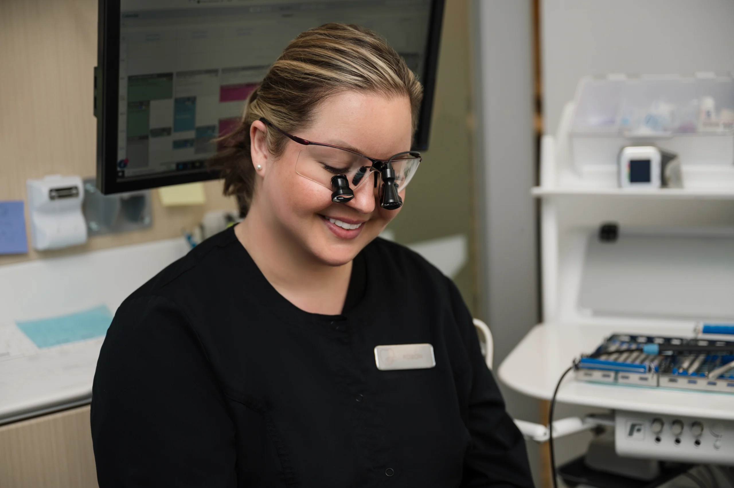 Robon wearing magnification glasses, looking down and smiling in an exam room