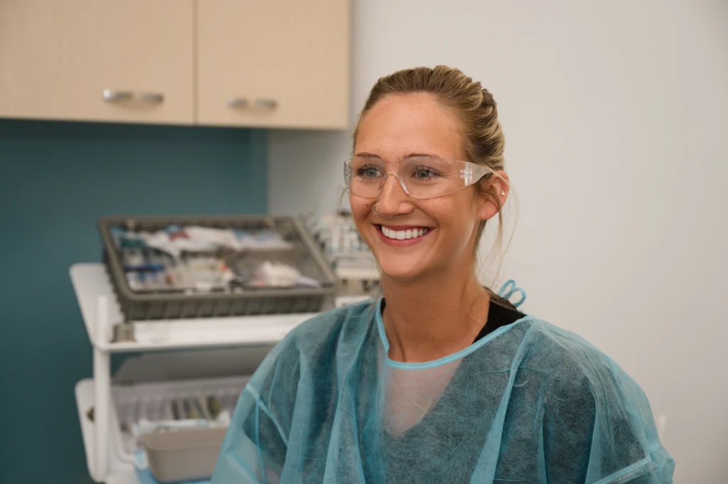 Trystan wearing safety glasses and a barrier jacket smiling in an exam room