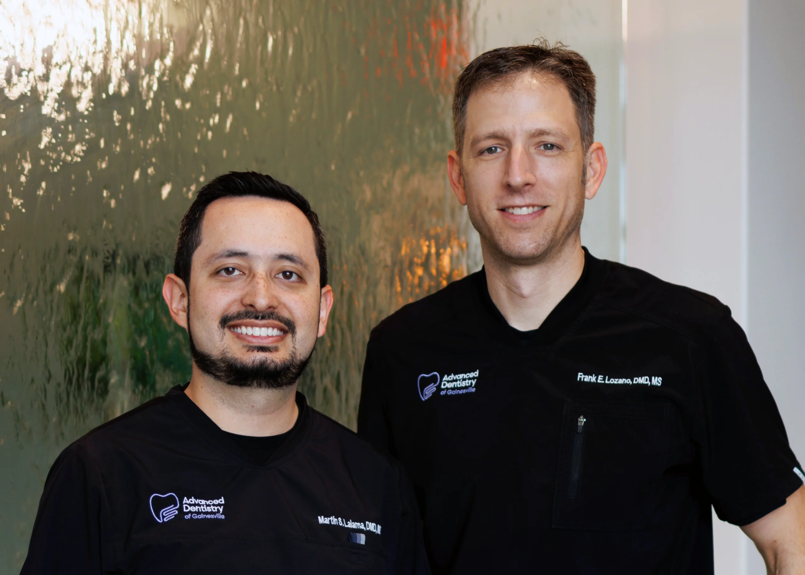 Dr. Lalama (left) and Dr. Lozano (right) stand in front of the water feature in the lobby at Advanced Dentistry of Gainesville