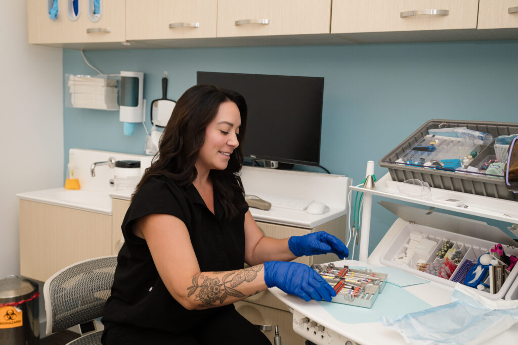 A worker wearing gloves in a clean exam room handling a tray of equipment